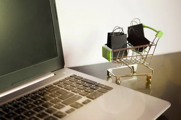 Shopping cart miniature with bags stand near laptop. Black friday banner. Sale announcement. E-commerce business.