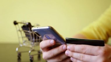 Kredi kartıyla internetten satın almak. Akıllı telefonu tutuyorsun. Çantalı alışveriş arabası. İnternetteki mağaza. Kara Cuma indirimi. Boşluğu kopyala