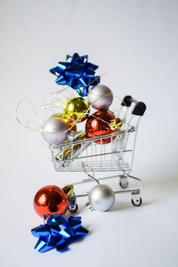Noel dekoru alışveriş arabasında. Yeni yıl terfileri. Toplar ve kurdele. Beyaz arka plan. Ailene hediye al. Dikey yönelim