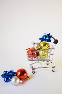 Noel dekoru alışveriş arabasında. Yeni yıl terfileri. Toplar ve kurdele. Beyaz arka plan. Ailene hediye al. Dikey yönelim