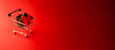 Hediye paketi alışveriş arabasında. Noel indirimi afişi. Uzayı kopyala Maytap bulanık. Kırmızı arka plan. Yeni Yıl Kutlaması