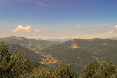 Bir yaz günü doğal görünümünü bir kıyı kenti yakınında yeşil tepeler ve dağ ile mavi göl ve mavi gökyüzü bulutlu görünür