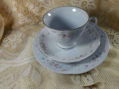 Üç parça kahvaltı Kupası küçük yarım kalp şekli kolu, dalgalı kenarlı tabak ve plaka ile oluşan küme diğer bir dantelli unicolored, Fildişi, çiçekli masa örtüsü oturan birinde stoklanmayacaktır çiçek beyaz boş. Tablo set kenarları altın gibi.