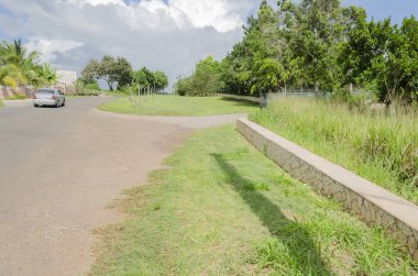 Araba bakımlı çimenli kaldırım yalnız cadde boyunca ilerledikçe kalın büyük bulut ile güneşli bir gün mavi gökyüzü altında asılı puffs. Uzun çim ve ağaçların düşük bakımlı çimenli yürüyüş alanı özel Binası bölen düşük kesme taş duvar.