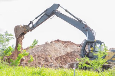  Sarı ve siyah Ekskavatör kova için bir yığın, kırmızı terra rossa kil toprak boşalma kazı konumunda kazdık alanından scooped.