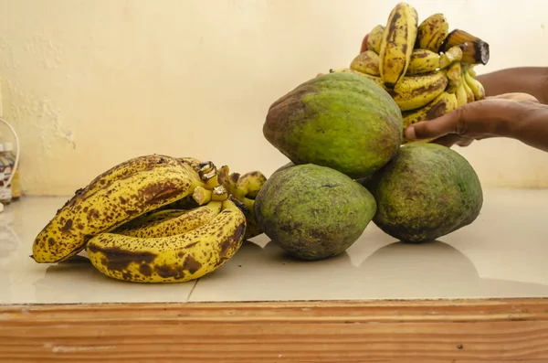 在白色瓷砖台面表面是棕色斑点 黄色成熟的香蕉 和绿色皮肤成熟的鳄梨 非常成熟的香蕉也手握 — 图库照片