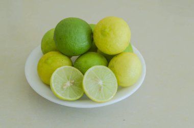 Sarı olgun ve yeşil olgun anahtar kireç meyve çanak çömlek ve beyaz kiremit yüzeyi arasında çıkıntılı ağacın yaprakları ile küçük bir beyaz plaka içinde.