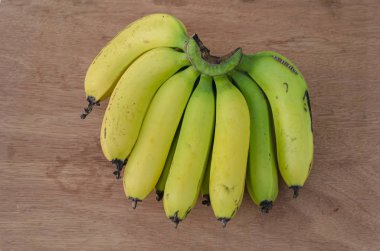 Kahverengi bir arka planda, sarı olgun muzlarla izole edilmiş bir el ve kısmen yeşil olgunlaşmamış meyveler var..