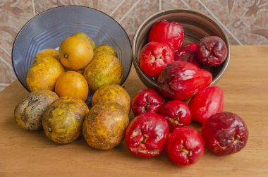 Bir tahta yüzeyinde bütün sarı olgun erik tabakları ve kırmızı olgun Otaheite elmaları var..