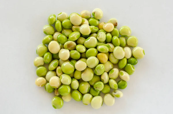 Green and white pigeon peas grains are gathered together on a white surface.