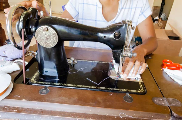 With one hand on the machine wheel, and the other at the front of the presser foot, a seamstress guides the fabric as it is being stitched by an old sewing machine.