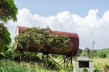 Bir zamanlar topluma su ile hizmet eden eski yuvarlak bir metal su varili, ağaçların arasında terk edilmiş olmasına rağmen hala ayakta duruyor..