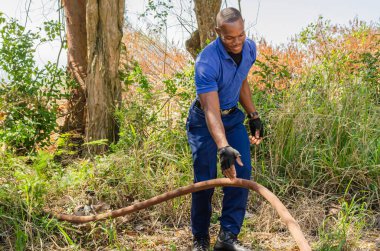 Çalı yangını var. Kamyon yaklaşamıyor, bu yüzden yangın yerine ulaşmak için fazladan hortum uzunluğuna ihtiyaç var. İtfaiyeci ekibi fazladan hortumla besledi ve elinden düşürmeye çalışıyor..
