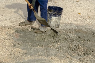 İnşaat alanında mavi tulumlu bir adam çimento ve marl toplamından yapılmış havanı karıştırmak için kürek kullanır. Havan yatağının yanında koyu mavi plastik bir kova var..