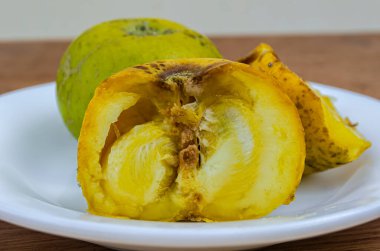 Beyaz tabakta bir bütünün meyveleri ve iki yarım olgunlaşmış beyaz saman vardır. Yarısı ön cephede, yuvarlak tohumlarını gösteriyor..