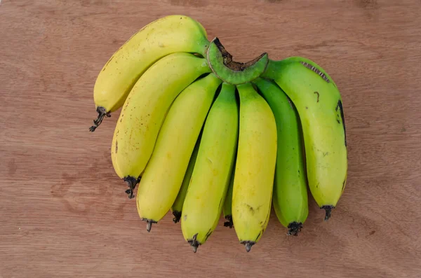 在棕色的木板背景上是一只孤立的手 有黄色成熟的 部分为绿色的未成熟果实的香蕉 — 图库照片