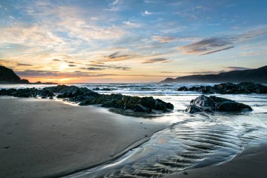 This is a pictur of a stream on a beach in Donegal Ireland at sunset. Sea cliffs can be seen in the distance. clipart