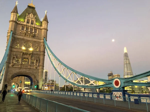 This a picture on hte deck of Tower Bridge in London.  It was taken at sunrise.  The moon and the London skyline can be seen in the distance.