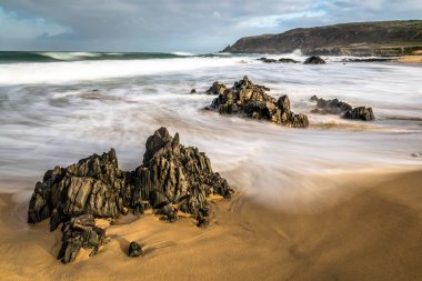 Bulanık dalgalar kayaların İrlanda kumlu bir plaj üzerinde çevresinde swirling.