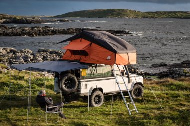 Clifden, Ireland- 25 Temmuz 2020 İrlanda 'nın batı kıyısında çatı çadırlı bir Land Rover' da kamp yapan bir adam.
