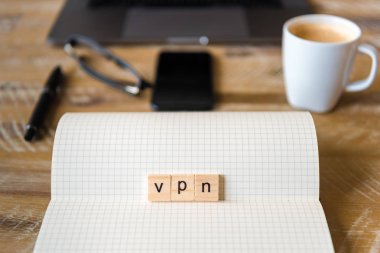 Closeup dizüstü ahşap masa arka plan, üzerinden Vpn kelime yapma harflerle ahşap bloklar üzerinde odaklanın. İşletme kavramı resmi. Dizüstü bilgisayar, gözlük, kalem ve ufuk arka plan içinde hareket eden telefon.