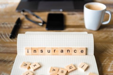 Dizüstü üzerinde ahşap masa arka plan, closeup sigorta kelime yapma harflerle ahşap bloklar üzerinde odaklanın. İşletme kavramı resmi. Dizüstü bilgisayar, gözlük, kalem ve ufuk arka plan içinde hareket eden telefon.