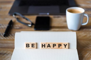 Closeup üstünde defter üzerinde ahşap masa arka plan, Be Happy kelime yapma harflerle ahşap bloklar üzerinde odaklanın. İşletme kavramı resmi. Dizüstü bilgisayar, gözlük, kalem ve ufuk arka plan içinde hareket eden telefon.