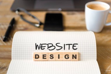 Closeup dizüstü ahşap masa arka plan, üzerinden Web sitesi tasarımı metin yapma harflerle ahşap bloklar üzerinde odaklanın. Kavram görüntü dizüstü bilgisayar, Gözlük, kalem ve cep telefonu ufuk arka planda