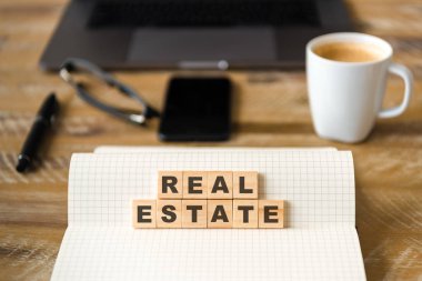 Dizüstü üzerinde ahşap masa arka plan, closeup Emlak metin yapma harflerle ahşap bloklar üzerinde odaklanın. Kavram görüntü. Dizüstü bilgisayar, Gözlük, kalem ve cep telefonu ufuk arka planda