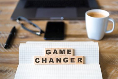 Closeup dizüstü ahşap masa arka plan üzerinde oyun değiştirici metin yapma harflerle ahşap bloklar üzerinde odaklanın. Kavram görüntü. Dizüstü bilgisayar, Gözlük, kalem ve cep telefonu ufuk arka planda