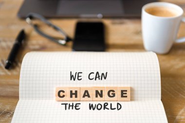 Closeup üstünde defter üzerinde ahşap masa arka plan, We Can Change The World metin yapma harflerle ahşap bloklar üzerinde odaklanın. Kavram görüntü. Dizüstü bilgisayar, Gözlük, kalem ve cep telefonu ufuk arka planda