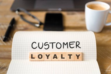 Closeup dizüstü vintage Resepsiyon yüzey üzerinde müşteri sadakati metin yapma harflerle ahşap bloklar odaklanmak ön. İşletme kavramı resmi office araçları ve kahve fincanı arka planda