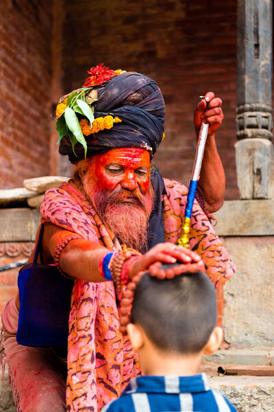 Pashupatinath, Nepal - July 17, 2018 : Holy Sadhu man with traditional painted face and colouful clothes is blessing a child at Pashupatinath, a famous and sacred Hindu temple complex in Nepal