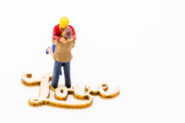 Minyatür figürler beyaz arka plan üzerinde izole metin aşk, ahşap işaretiyle yanındaki çift sarılma sevgi olduğu gibi