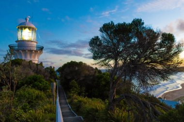 Sugarloaf Point Seal Rocks, Myall Lakes Ulusal Parkı, Yeni Güney Galler, Avustralya'daki deniz fenerinden sahile bakan gün batımı doğa manzarası
