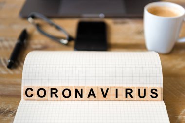 Ahşap masa arkasındaki deftere yakın çekim, Coronavirus 'un yazdığı harflerle tahta bloklara odaklan. Bilgisayarlı, gözlüklü, kalemli ve cep telefonlu iş kavramı