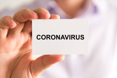İş adamının elinde Coronavirus metni olan bir kart tutmasına yakın plan, yumuşak odaklı arka planı olan iş konsepti resmi