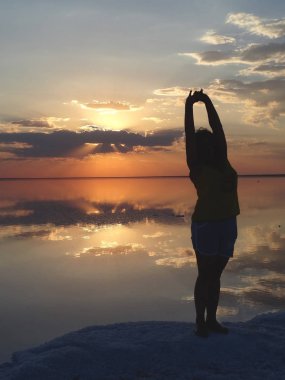 Bir adamın ellerini gökyüzüne bir turuncu günbatımı Elton Tuz Gölü yüzeyi yansıtan arka planı doğru çekerek anahat
