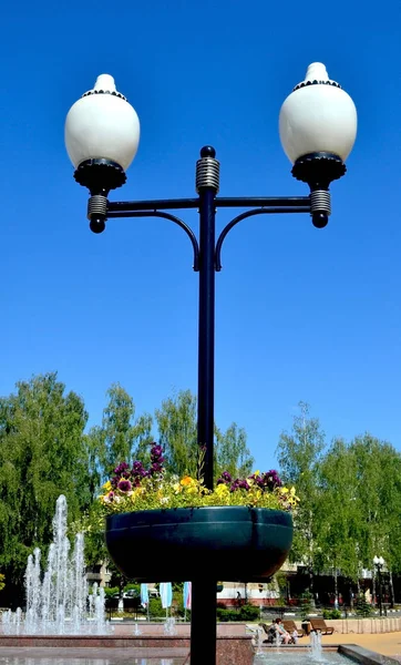 White street lanterns on a metal pillar against a blue sky background