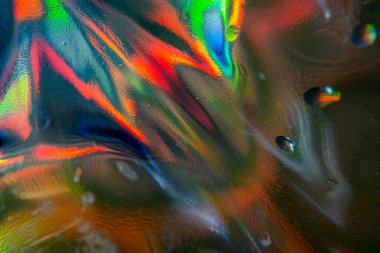 Doğrudan ışık altında parlak bir kristal cam yakın plan, kırmızı, mavi, yeşil, sarı ve turuncu renkli dairesel merkezli ışık kırıntılarını ve soyut desenleri gösterir..