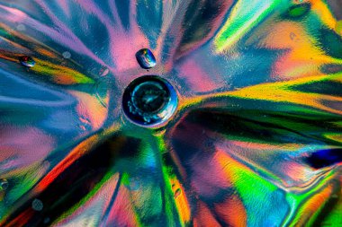 Doğrudan ışık altında parlak bir kristal cam yakın plan, kırmızı, mavi, yeşil, sarı ve turuncu renkli dairesel merkezli ışık kırıntılarını ve soyut desenleri gösterir..