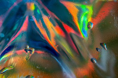 Doğrudan ışık altında parlak bir kristal cam yakın plan, kırmızı, mavi, yeşil, sarı ve turuncu renkli dairesel merkezli ışık kırıntılarını ve soyut desenleri gösterir..