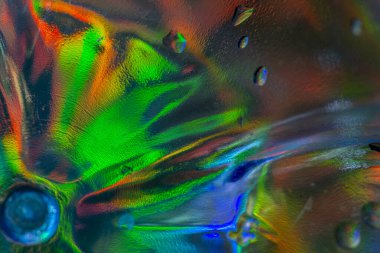 Doğrudan ışık altında parlak bir kristal cam yakın plan, kırmızı, mavi, yeşil, sarı ve turuncu renkli dairesel merkezli ışık kırıntılarını ve soyut desenleri gösterir..