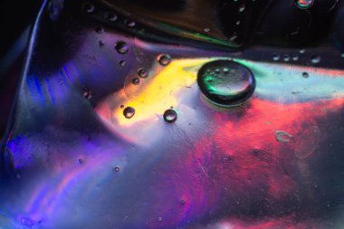 Mor, mavi, sarı, yeşil ve kırmızı renkli ışık çarpıtmaları ve sıvı desenleriyle canlı yansımaları gösteren desenli yüzeydeki renkli sıvı baloncukların soyut makro fotoğrafı..