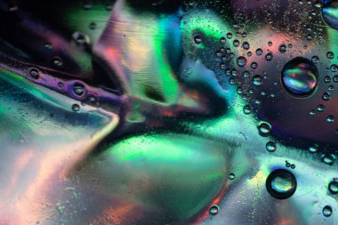 Yeşil, mavi, mor ve pembe karışımın canlı renkleriyle pürüzsüz bir yüzey üzerinde sıvı baloncukların soyut makro fotoğrafı, parlak yansımalar ve sıvı dokular yaratır..