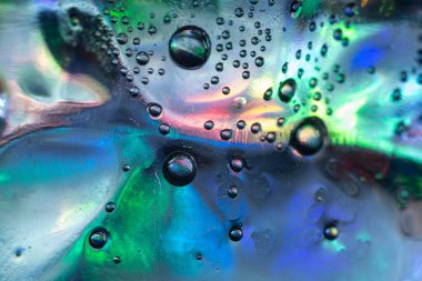 Yeşil, mavi, mor ve pembe karışımın canlı renkleriyle pürüzsüz bir yüzey üzerinde sıvı baloncukların soyut makro fotoğrafı, parlak yansımalar ve sıvı dokular yaratır..