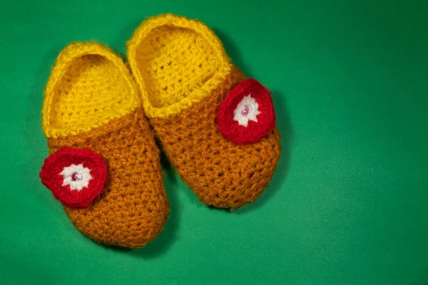 colorful knitted baby Slippers with a red flower on a green background