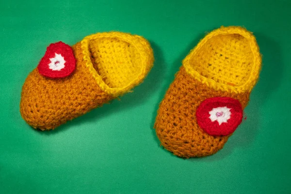 colorful knitted baby Slippers with a red flower on a green background