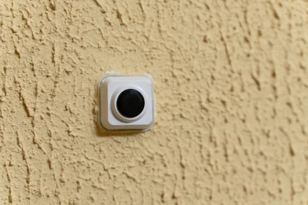 black doorbell button in white case on yellow wall with embossed texture