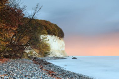 Sonbahar gündoğumu Baltık Denizi uçurumlarda tebeşir. kırmızımsı bulutlar gökyüzü döner. Ağaçlar ve çalılar - Doğa Park alanı jasmund ile doğal bir plaj ön planda olduğunu